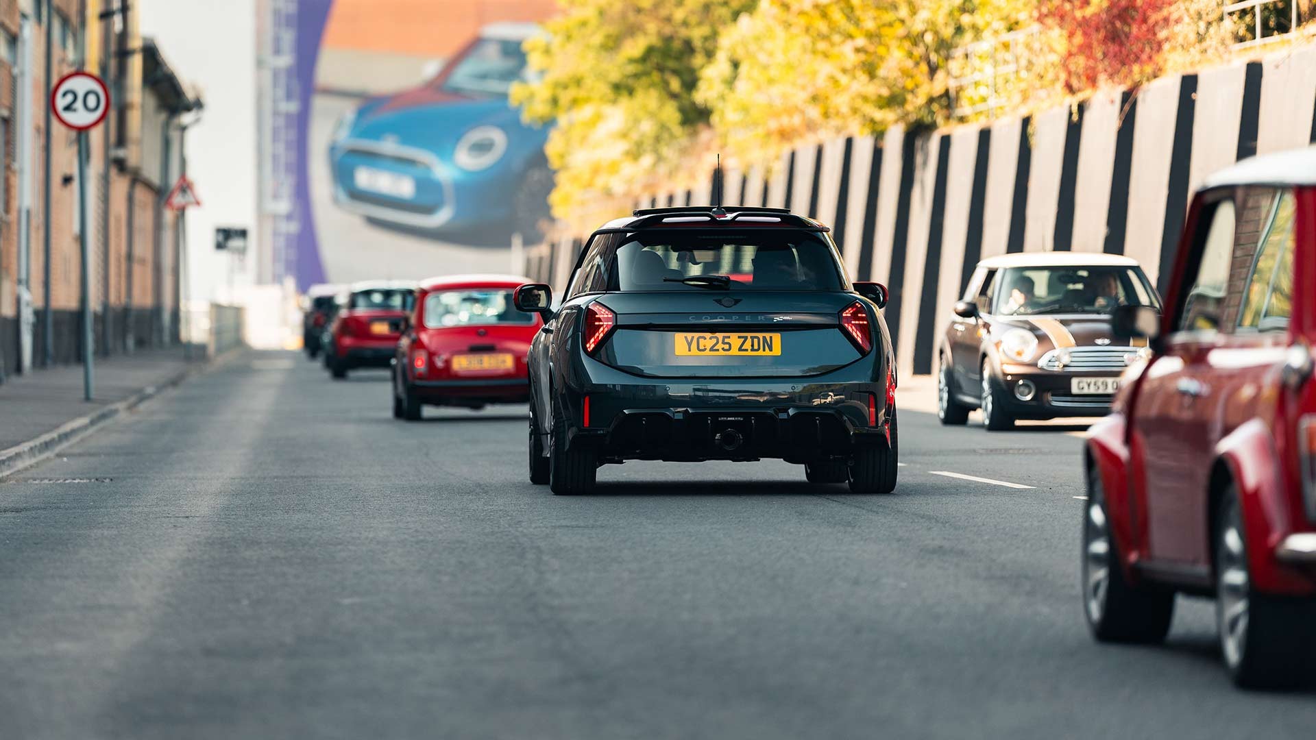 Street scene with several cars driving past a brick building and colorful billboard. 